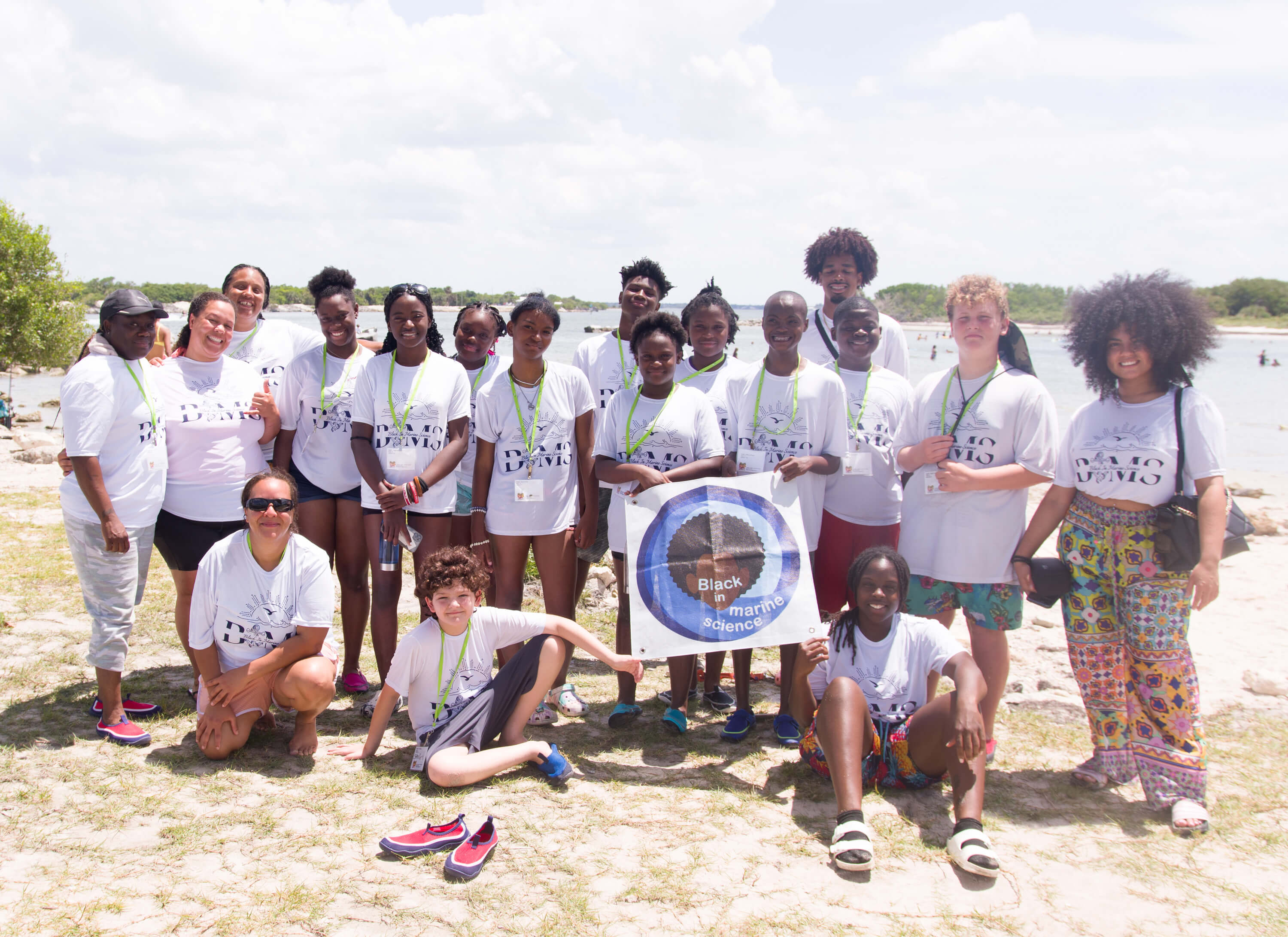 A group of students and staff pose on the beach with a Black in Marine Science flag.