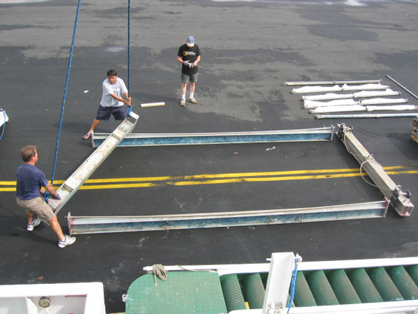 The frame of the MOC 10 trawl is bolted together on the dock next to the ship.