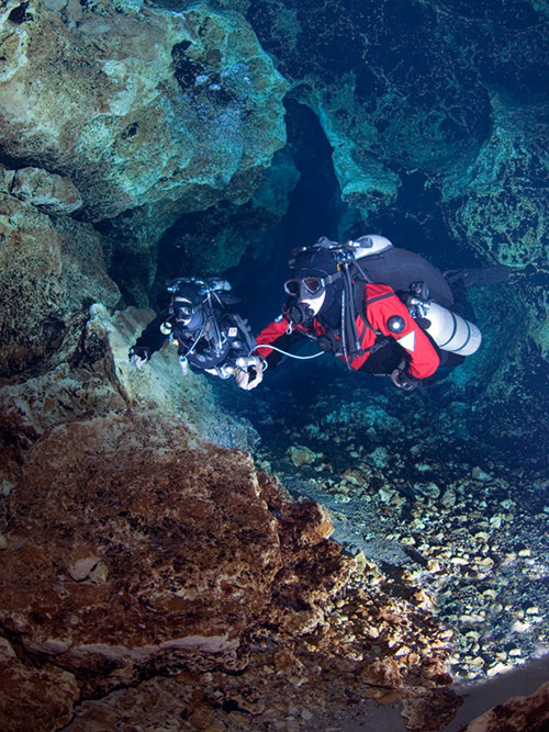 Two divers using traditional back mounted open circuit scuba equipment to explore a cave.