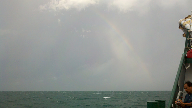 David Ulloa records video while a rainbow breaks through the clouds behind him.