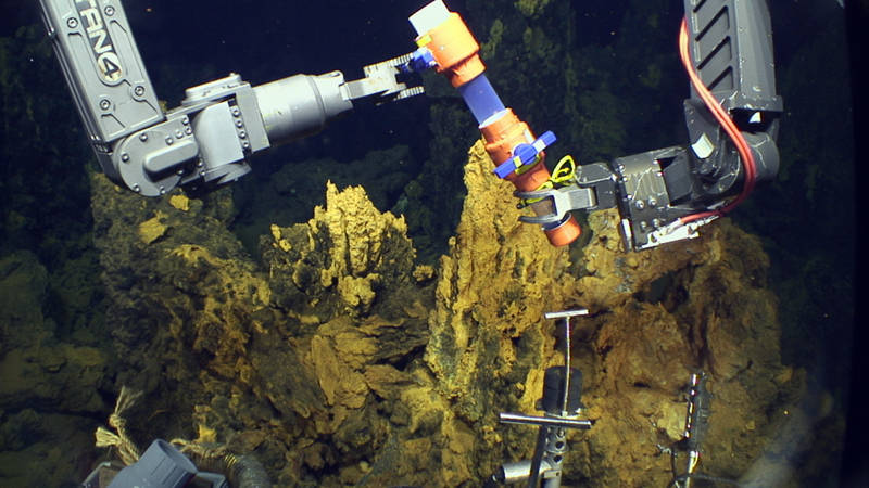 Jason opens a valve at the top of one of the scoop samplers before taking a sample of microbial mat from the chimneys in the background.