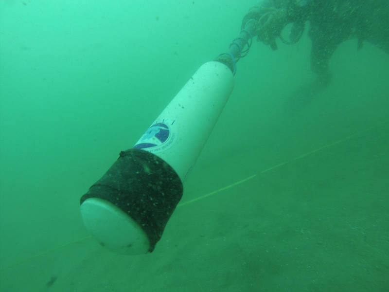 I am the diver in this picture, extending the head of the handheld magnetometer in front of my body and sweeping it along the seafloor while looking and listening for changes in readings which might signify buried iron wreckage.