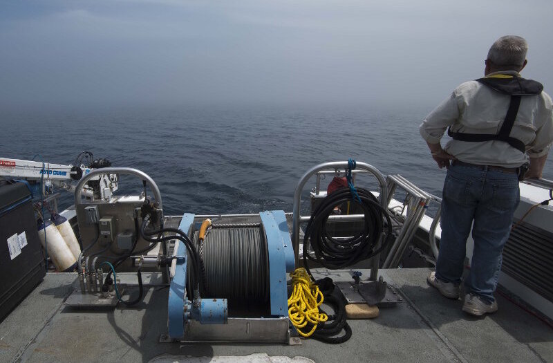 Co-Principal Investigator Dr. Art Trembanis sits watch with University of Delaware doctoral student Carter DuVal. Together, they monitor incoming sonar data and Project PI Dr. Guy Meadows looks across the lake surface into a dense fog surrounding R/V Storm. As the AUV missions progressed, the vehicle would periodically surface to update its GPS position. In addition to establishing a wireless connection, the survey team would also attempt to get visual confirmation of the vehicle’s status. This was extremely challenging, however, when socked in with fog.