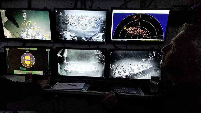 Structure of shipwreck visible on scanning sonar (display at top right) while ROV operator Paul Sanacore prepares to collect a sediment core with the manipulator arm.