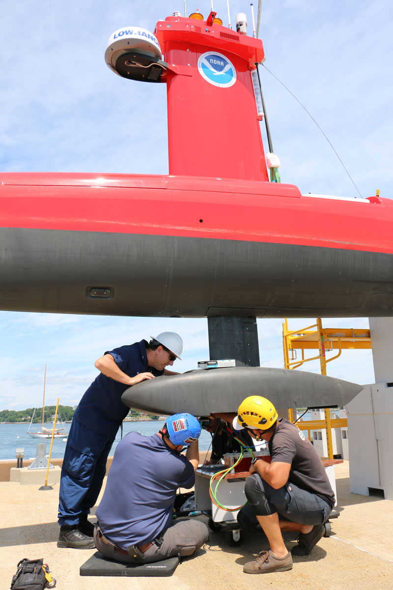 Three people performing maintenance on a part of the DriX.