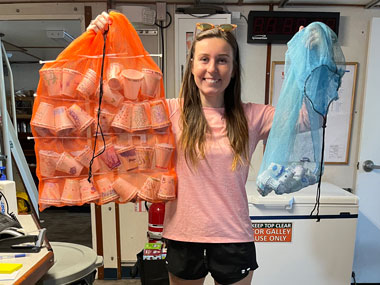 Courtney Brooks with a bag of cups ready to be attached to the remotely operated vehicle and sent to the deep for shrinking (orange) and a bag of cups that were already shrunk (blue).