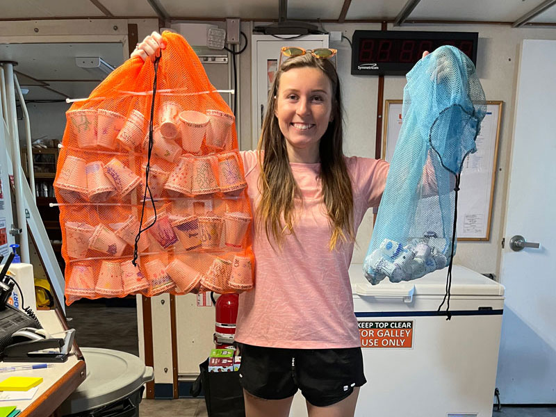 Courtney Brooks with a bag of cups ready to be attached to the remotely operated vehicle and sent to the deep for shrinking (orange) and a bag of cups that were already shrunk (blue).