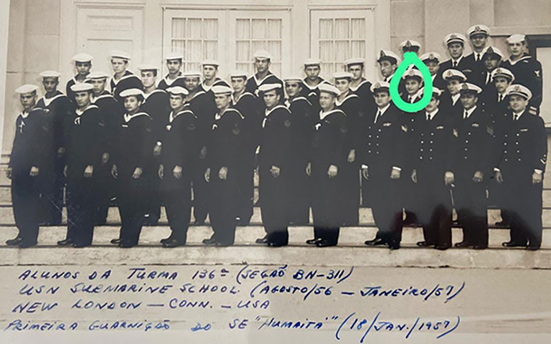 Group of naval officers and sailors in uniform posed on stairs with one person highlighted.