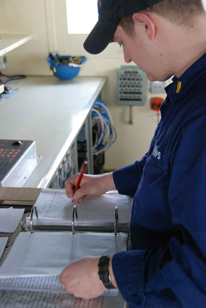 ENS Benjamin Bloss writes in one of the many logs that the bridge officers must update during their watches. These include the deck, VHF, GMDSS, compass, trash, and weather logs.