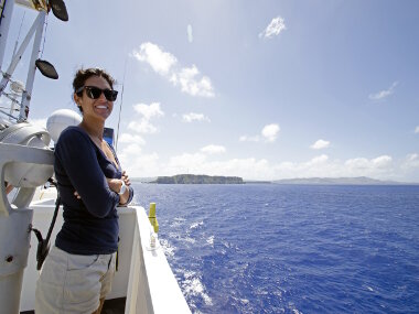 Leg 1 Biology Science Team Lead, Dr. Diva Amon, enjoying the view as NOAA Ship Okeanos Explorer heads to sea to start Leg 1 of the 2016 Deepwater Exploration of the Marianas Expedition. You can see the island of Guam in the background.