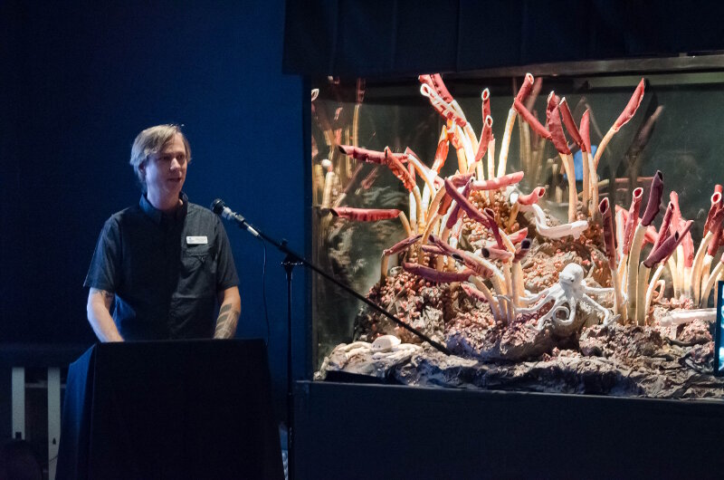 Mike McCue, the head curator for UnderwaterWorld Guam, gives remarks during an opening event to debut their newly established Exploration Command Center. Additional exhibits relevant to the 2016 Deepwater Exploration of the Marianas expedition have been developed or are in the works, such as the hydrothermal vent tubeworm community display on the right.