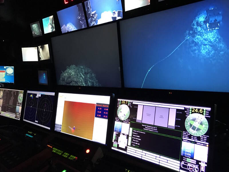 Pilot displays showing orientation, depth, and distance from bottom of D2 and Seirios, sonar from each, and their relative relation to the ship (orange chart). Large monitors above show main cameras from D2 and context view from Seirios.