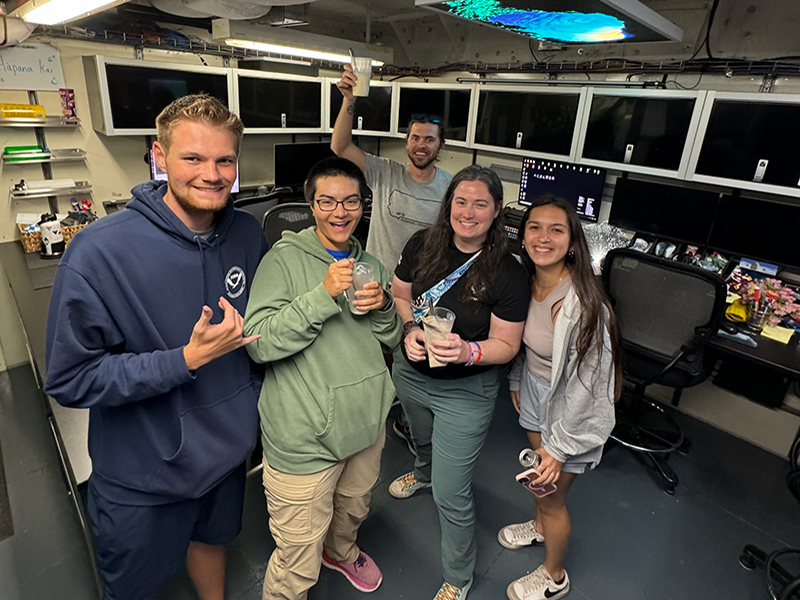 Image of cultural liaison Makoa, explorer-in-training Elizabeth, media specialist Nate, watch lead Mia, and explorer-in-training Anabel in the dry lab of NOAA Ship Okeanos Explorer after a milkshake delivery for those still working into the night.