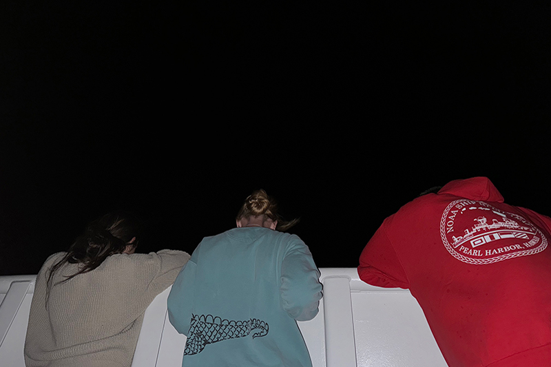 Explorer-in-training Anabel, sample data manager Jennifer, and cultural liaison Makoa leaning on the starboard side of the ship’s bow searching for bioluminescence in the water!