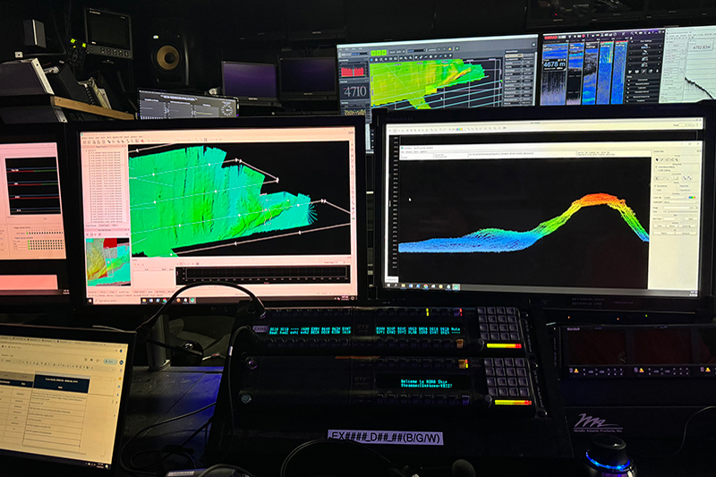 Image of one of the working stations in the mission control room. There are three working stations with two monitors for each station. On the left screen, you can see some of the colorful mapped data along the ship’s mapping route. The ship moves like a lawnmower to map the large area and you can see that pattern with the white lines with arrows. On the right screen, you can see what the data looks like for the watch standers who are responsible for monitoring the technology and cleaning the data. The machine right under the two screens is the radio which is used to communicate with the bridge, the area of the ship in charge of steering.