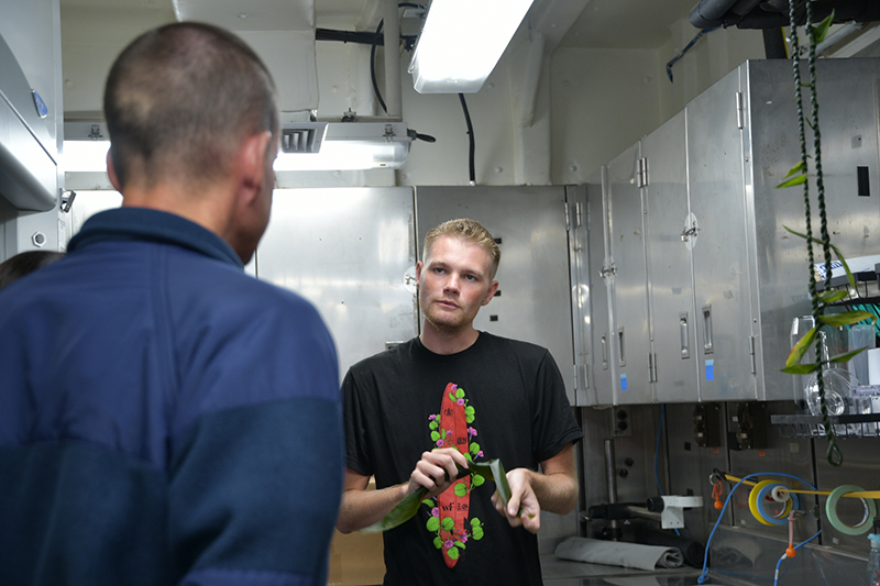 Makoa Pascoe, who is serving as a cultural liaison during the Beyond the Blue: Papahānaumokuākea Mapping 1 expedition, teaches members of NOAA Ship Okeanos Explorer’s crew how to make lei lā’ī of ti leaves. Prior to the ship’s departure, the cultural liaison team prepared a lei lāʻī for placement on the ship’s bridge rail as part of an Oli Pale to seek protection while underway. Many members of the on-ship team hung the leis they made on their stateroom doors.