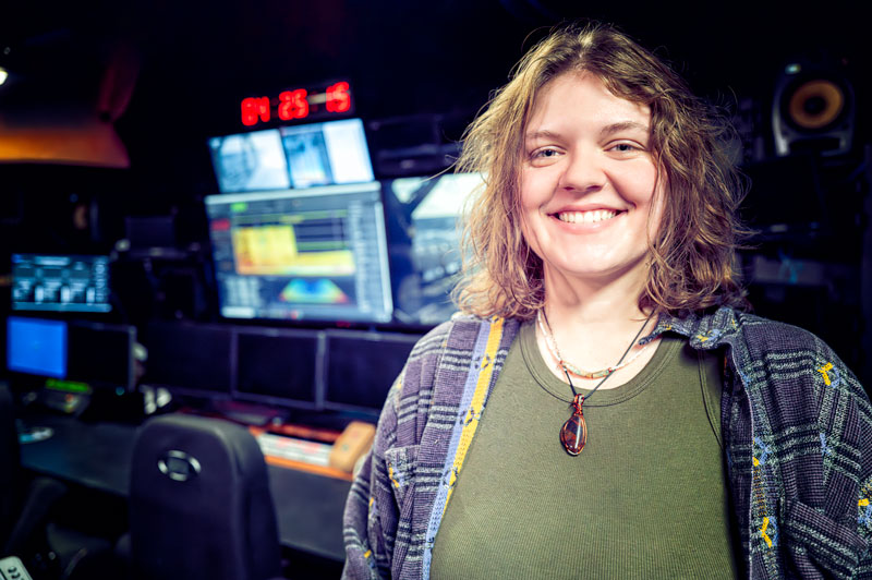 Person smiling in a control room with multiple monitors displaying data.