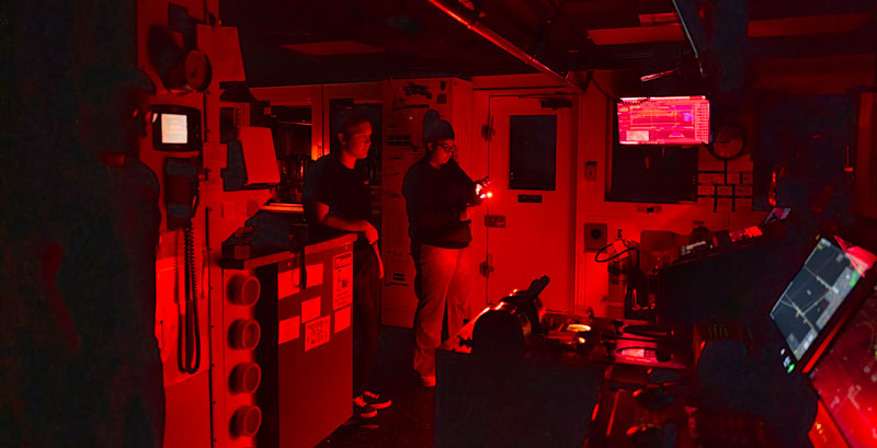 Person smiling in a control room with multiple monitors displaying data.