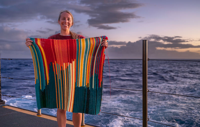 NOAA Ocean Exploration Internship Program Coordinator Jesse Gwinn on the fantail of NOAA Ship Okeanos Explorer with her in-progress bathymetry blanket, which illustrates ocean depth data collected during the Beyond the Blue: Johnston Atoll Mapping 2 expedition.